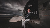 Teenage male sitting in the Wrecked DC-3 Plane on Sólheimasandur with dramatic sky looking away