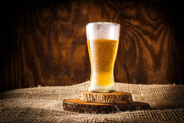 glass with beer and foam on dark rustic wooden background and sack background - rustic beer brewery indoors imagens e fotografias de stock