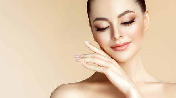 Gorgeous young woman with clean fresh skin is touching the face.  Light smile on the perfect face. Cosmetology. stock photo