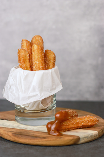 Churros with sugar and caramel sauce in a glass, grey table with copy space