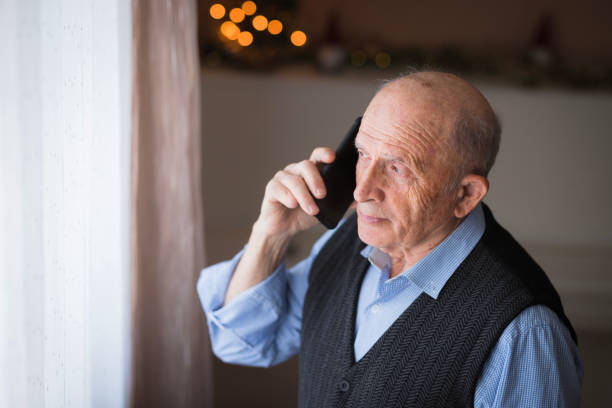 Elderly man having a phone conversation with his family on a Christmas morning via mobile phone at home