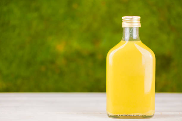 Yellow drink - homemade ginger shot, citrus juice or lemonade in glass bottle. Green background. Immunity boosting healthy drink. Copy space for text.
