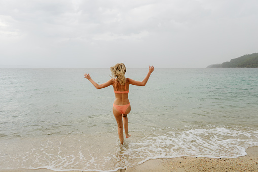 Photo of a young woman enjoying the last days of summer at the beach and swimming in the ocean on a gloomy day.