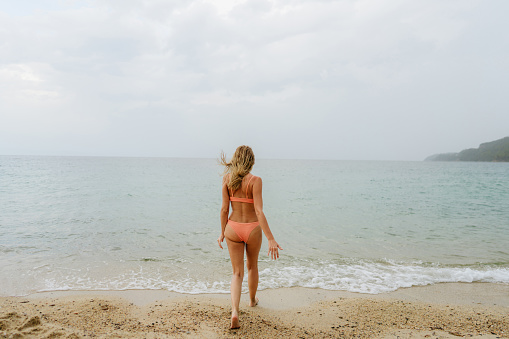 Photo of a young woman enjoying the last days of summer at the beach and swimming in the ocean on a gloomy day.