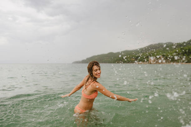 Photo of a young woman enjoying the last days of summer at the beach and swimming in the ocean on a rainy day.