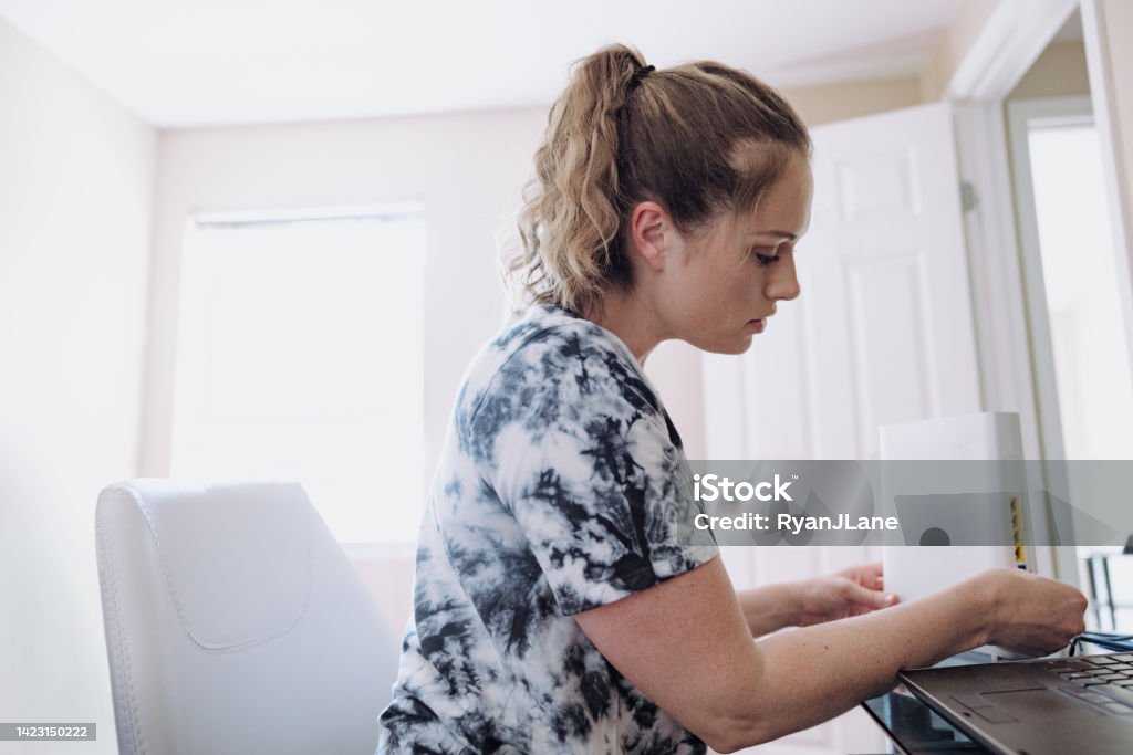 Woman Connecting Router In Home Office A mid-adult Caucasian woman sets up her wireless network at home in the computer room. Router Stock Photo