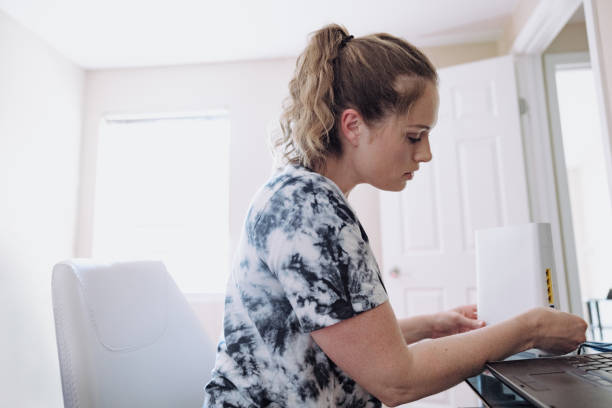 Woman Connecting Router In Home Office A mid-adult Caucasian woman sets up her wireless network at home in the computer room. router stock pictures, royalty-free photos & images