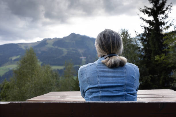 A gray-haired woman sits on a bench all alone. Austria, Salzburg. High quality photo