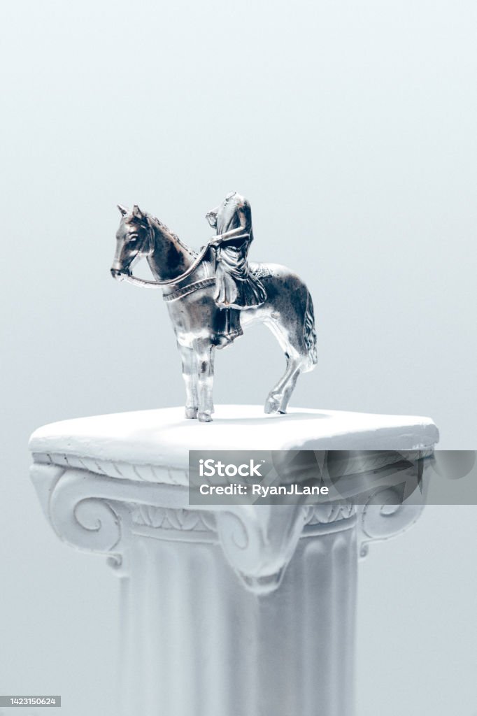 Headless Horseman Figurine on White Pedestal An old metal figurine of a king riding a horse, but the rider has literally lost their head.  Symbolism of failed or toppled leadership, presidency, politician, ideology, or other human failure or problem. Bizarre Stock Photo