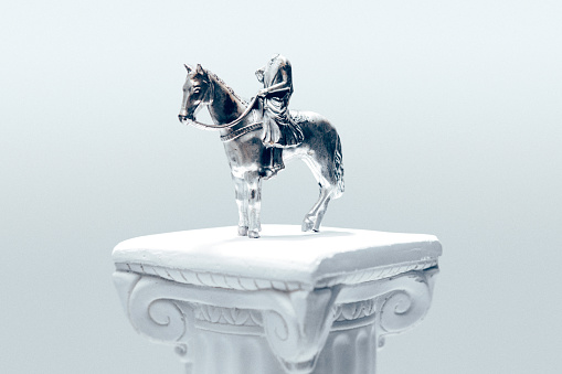 An old metal figurine of a king riding a horse, but the rider has literally lost their head.  Symbolism of failed or toppled leadership, presidency, politician, ideology, or other human failure or problem.