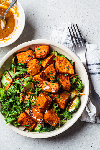 Baked sweet potato and green salad bowl with mustard dressing, top view. Vegan food concept.