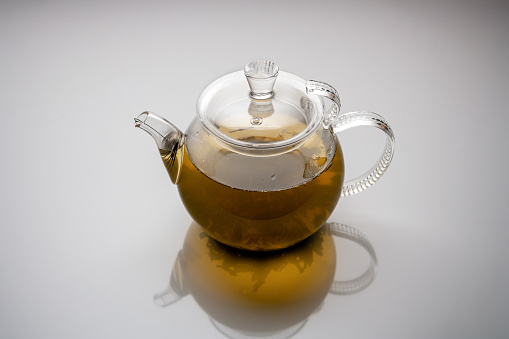 glass teapot with herbal tea reflected on white background