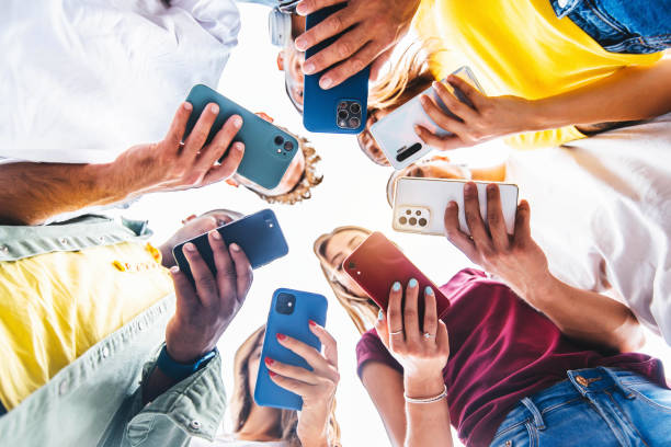 Teens in circle holding smart mobile phones - Multicultural young people using cellphones outside - Teenagers addicted to new technology concept stock photo
