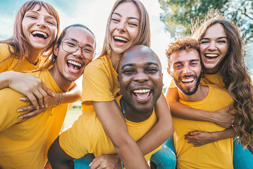 Multiracial community of young people smiling at camera outdoors - Happy students having fun together in college campus - Group of multicultural friends wearing yellow t shirts standing outside