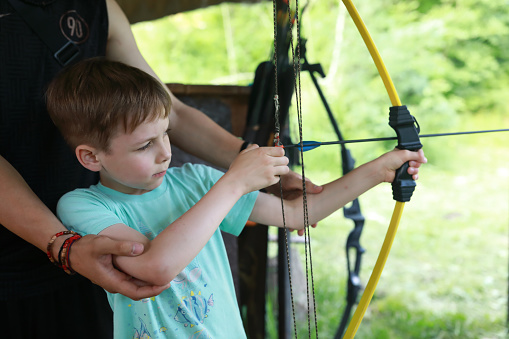 Instructor teaching boy to shoot bow in park