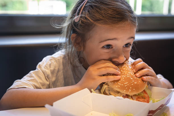 istock A little girl eats an appetizing burger, close-up. 1423163851