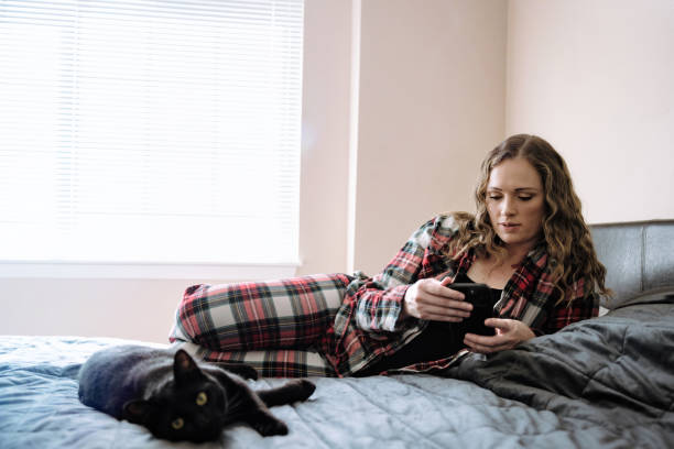 istock Woman Relaxing On Bed With Phone and Cat 1423164146