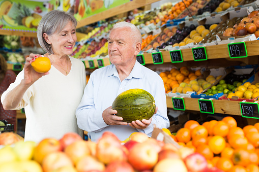 Elderly married couple choosing different fruits together in vegetable supermarket