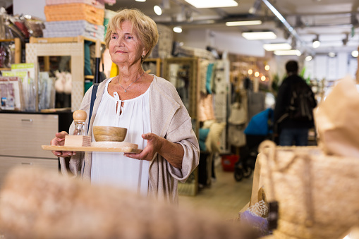 Senior woman customer holding purchases and walking in a household goods store
