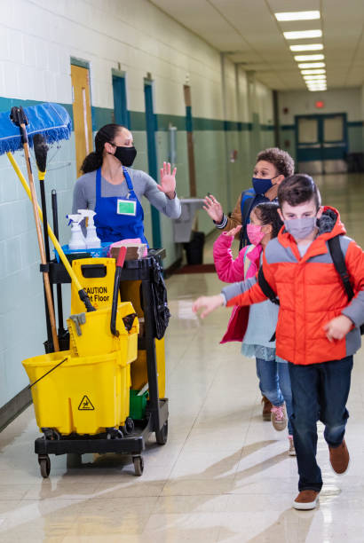 istock Children in school hallway wave hurrying by a janitor 1423165635