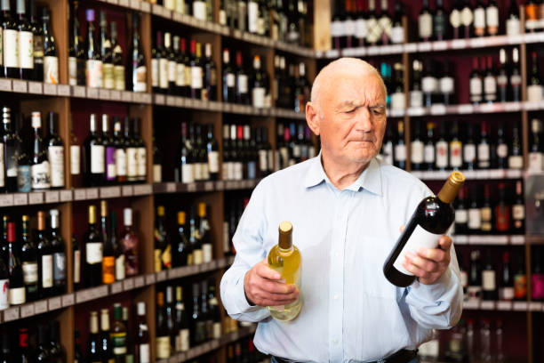 istock Serious elderly man chooses between red and white wine in a liquor store 1423165963