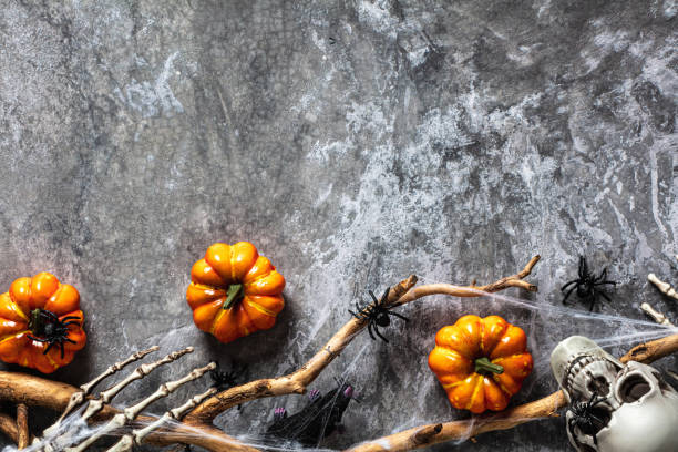 istock Spooky Halloween background with orange pumpkins, skeleton arms, skull, tree branch with web, spiders on stone desk table. Flat lay, top view, copy space. 1423167113