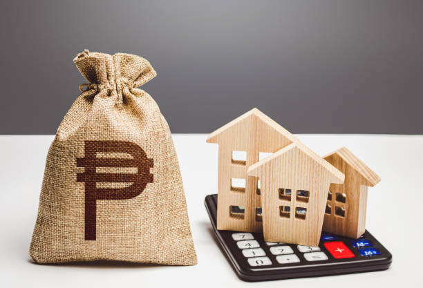 Houses on a calculator and philippine peso money bag. Realty or rental business. Buying and selling. Building maintenance. Real estate valuation. Mortgage loan. Utilities and services expenses. Taxes casas en una calculadora y bolsa de dinero en pesos filipinos. negocio inmobiliario o de alquiler. compra y venta. mantenimiento de edificios. valoración inmobiliaria. préstamo hipotecario. gastos de servicios públicos y servicios. impuestos