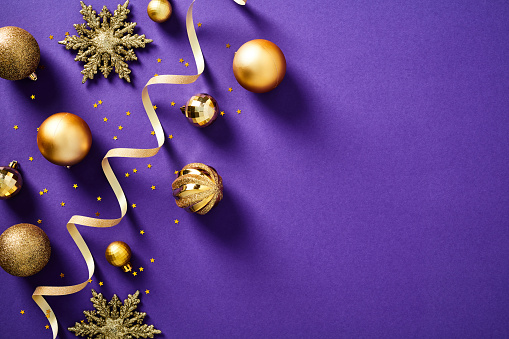 Luxury Christmas background with golden balls ornaments, snowflakes, ribbon, confetti stars on purple table. Xmas banner design, New Year greeting card mockup. Flat lay, top view.
