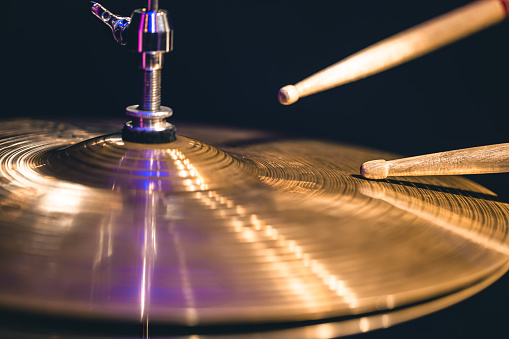 Hi-hat close-up of plates with drumsticks on a background of colored lanterns. Musical concept with a working drum.