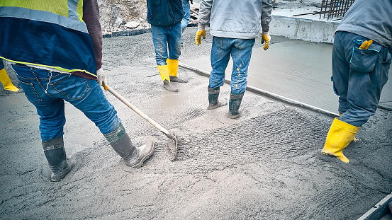 Construction worker uses bullfloat to spread cement mortar screed. Concrete works on construction site. Cast-in-place concrete works. Contractors spread grout using trowel