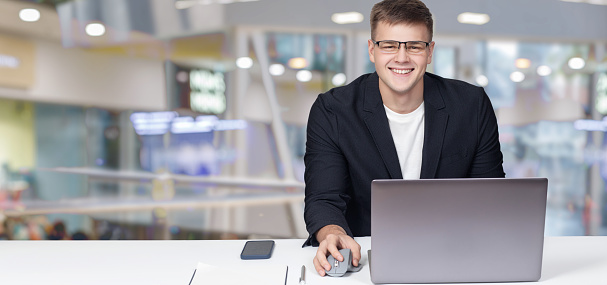 Young smiling businessman sitting at the table at the computer.