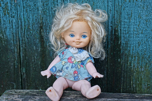 one plastic doll in a colored dress and white hair sits on a gray table against a green wall