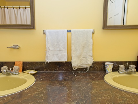 Depiction of domestic bathroom with a yellow theme. Bathroom counter and sinks with towel rack in dual mirrors with yellow painted walls. Room for copy.