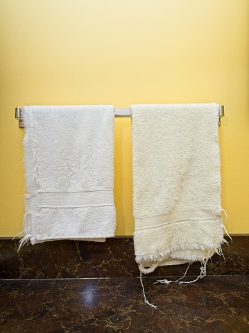 Frayed towels on rack in yellow domestic bathroom with formica marbled countertop. Ragged towels with copy space.