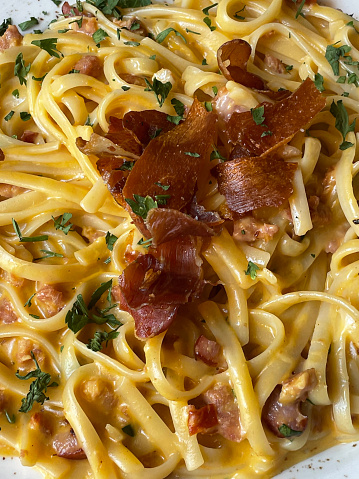 Stock photo showing elevated view of an Italian spaghetti carbonara recipe dish dining out at restaurant with pasta dish of spaghetti, chorizo, pancetta and mushrooms garnished with flat leaf parsley.