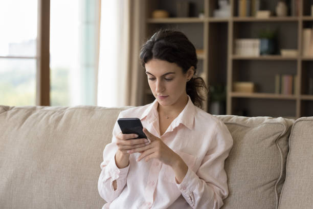 istock Serious woman sit on sofa holds smartphone share messages 1423181241