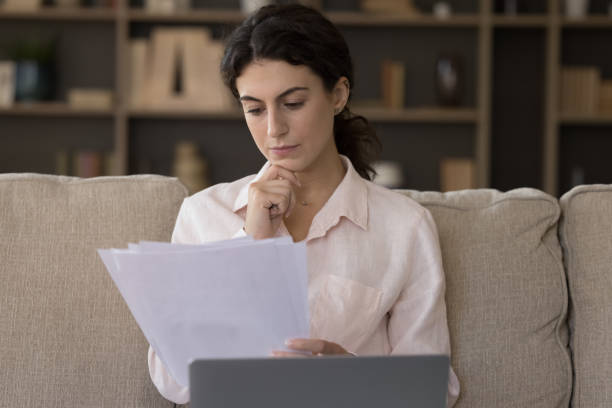 istock Serious woman working with correspondence seated on sofa with laptop 1423181437