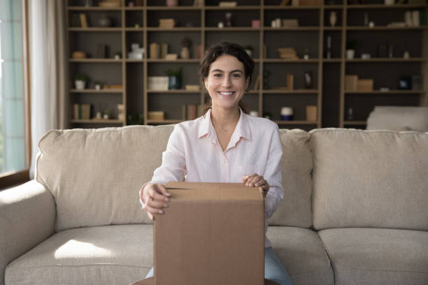 istock Woman sit on sofa with parcel smile look at camera 1423181445