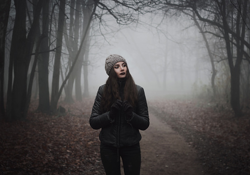 Girl on the scary road in the paranormal world. Strange forest in a fog. Mystical atmosphere. Dark wood. Mysterious road. Gothic witch. Background wallpaper. Gloomy times. Dark background