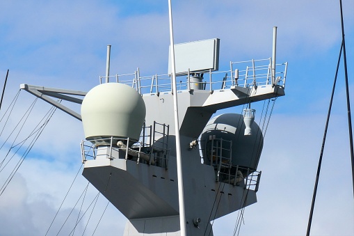 Radar and communications domes on a mast of HMAS Canberra of the Royal Australian Navy, moored at Garden Island in Sydney Harbour. This image was taken on an afternoon in Spring.