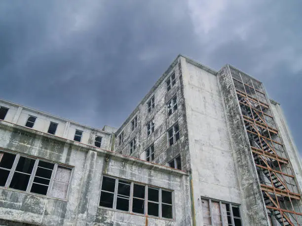 Dark ominous clouds and abandonment of old conrete industrial building from low point of view.