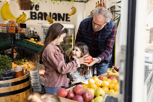 Two girls and their grandfather buying fruit and vegetable at the neighborhood grocery store