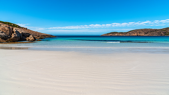 Horizontal landscape panoramic view of blue ocean waters, coastal scrub forest and a tranquil sandy beach under a clear blue sky. Pretty Beach, Meroo National Park, near Ulladulla, south coast NSW.