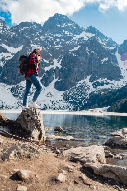 uma mulher está parada na margem de um lago. morskie oko, montanhas tatras. - tatra mountains zakopane lake mountain - fotografias e filmes do acervo