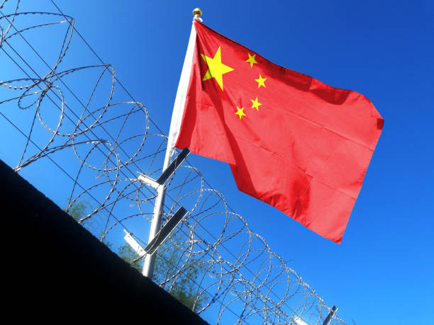 The Chinese flag hangs in the cloudy sky outside the prison's barbed wire. waving in the sky The Chinese flag hangs in the cloudy sky outside the prison's barbed wire. waving in the sky prc stock pictures, royalty-free photos & images