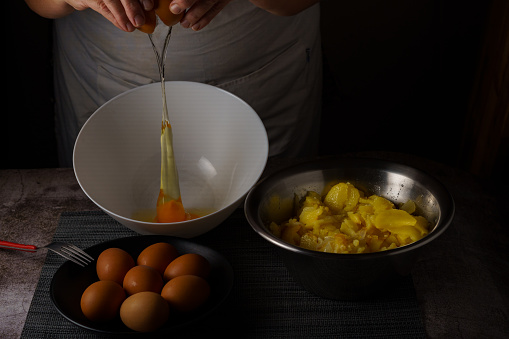 woman in white apron cracking eggs into a bowl with the ingredients for a potato omelet