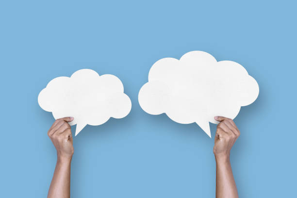 istock hand holding white paper cloud shape speech bubble balloon isolated on light blue background. 1423249086