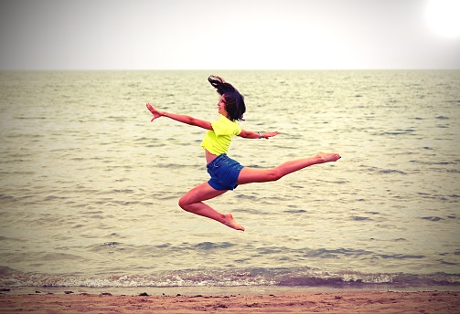 young girl jumping like a deet on the beach with toned effect in summer