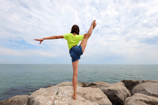 Young slender girl doing exercises on the rocks to keep fit by the sea