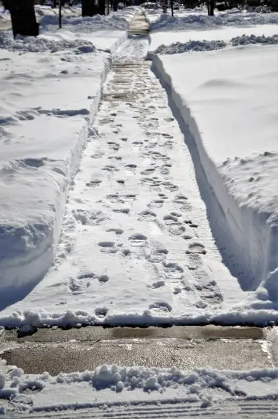 Photo of Footprints on the snow covered sidewalk in residential area.